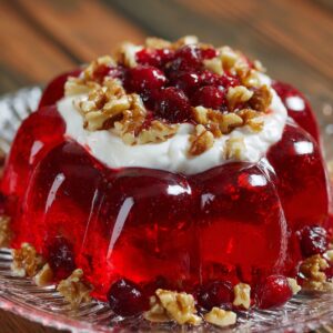 A gelatin Cranberry Jello Salad Recipe set in a molded shape, topped with whipped cream and garnished with cranberries and walnuts.