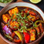 A bowl of Chili Paneer Recipe with golden paneer cubes, stir-fried onions and bell peppers in a glossy red sauce, garnished with fresh coriander leaves.