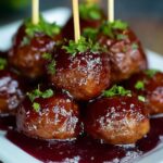 A bowl of grape jelly meatballs coated in a glossy sauce, garnished with fresh parsley.