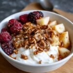 A bowl of Greek Healthy Yogurt Bowl Recipe with fresh raspberries, blackberries, diced apples, and crunchy granola.