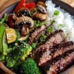 Bowl with Hibachi Steak Recipe – A wooden bowl filled with white rice, seared steak slices topped with sesame seeds and green onions, sautéed mushrooms, broccoli, zucchini, snap peas, and red bell peppers.