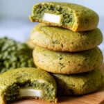 Four freshly baked Matcha Cookies Recipe stacked on top of each other, with a bite taken out of the top one to reveal a soft and gooey center.