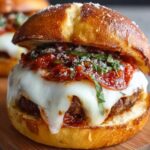 A mouth-watering Pizza Burger Recipe with melted mozzarella cheese, marinara sauce, and fresh basil on a soft pretzel bun.
