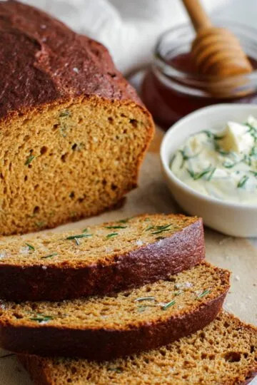 A loaf of rustic homemade outback bread recipe, partially sliced, served with a bowl of creamy herb butter and honey in the background.