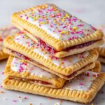 A stack of poptart recipe homemade frosted pastries with colorful sprinkles on top and jam filling peeking out from the layers.
