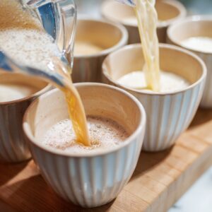 Pouring custard into cups – A creamy custard mixture is being poured into ceramic serving cups on a wooden board.