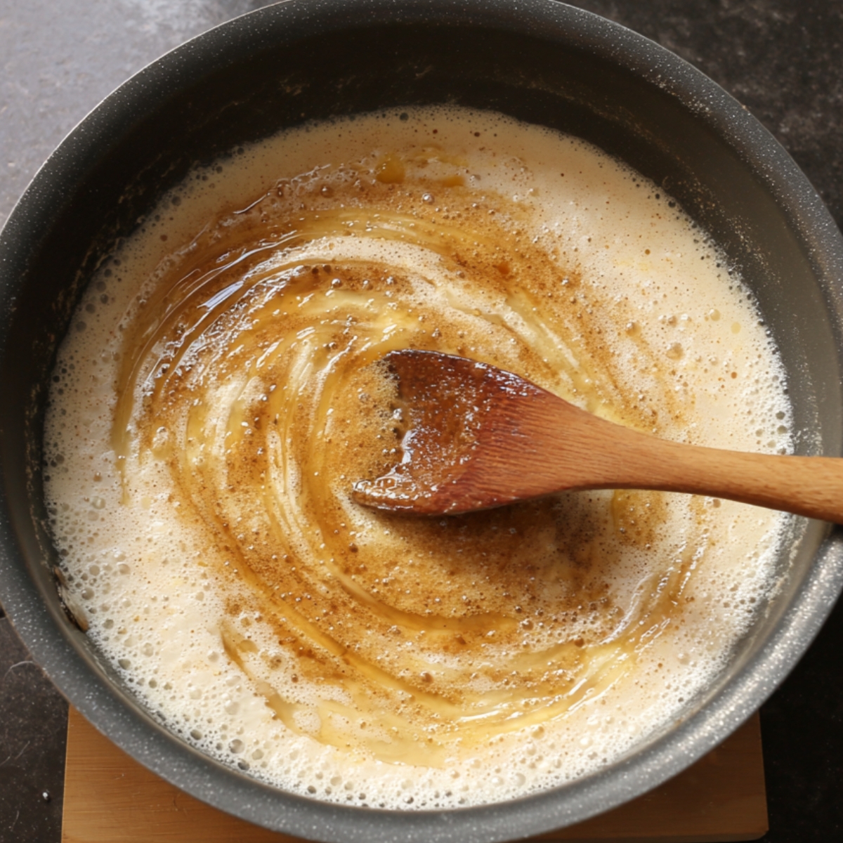Coconut milk and brown sugar mixture simmering in a pan, stirred with a wooden spoon.