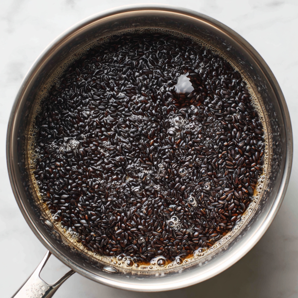 Black rice simmering in water inside a stainless steel pot.