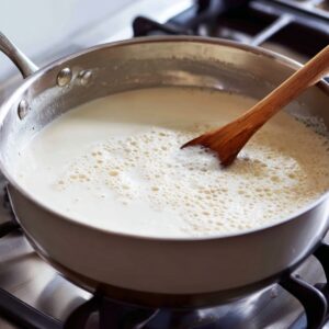 This step indicates adding milk to the pan to begin cooking the carrots for the dessert.