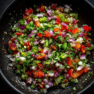A colorful mixture of diced red onion, peppers, tomato, and cilantro tossed together in a black bowl.