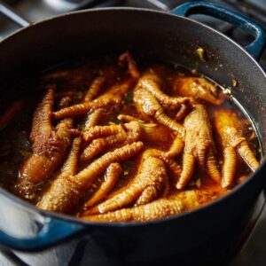 A deep blue cast-iron pot filled with chicken feet braising slowly in a brown, flavorful broth.