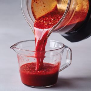 Preparing Chile Sauce: Blended red chile mixture being poured from a blender into a measuring cup, smooth and thick.
