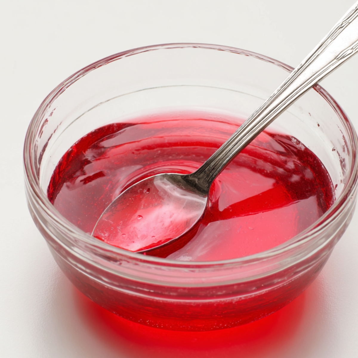 A clear, bright red gelatin base in a bowl, with a spoon resting in it.