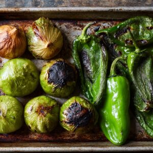 The first stage of preparing a verde salsa, where charred vegetables like onions and peppers are being blended together to create a flavorful base.