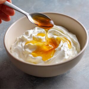 A spoon drizzling golden honey over a bowl of thick, creamy Greek yogurt.