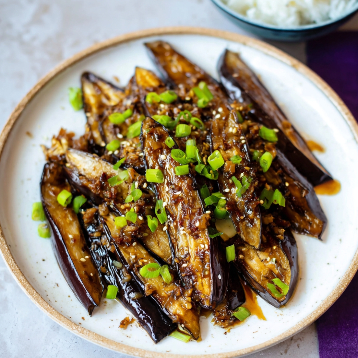 A plate of stir-fried eggplant with a glossy sauce, garnished with chopped green onions and sesame seeds.