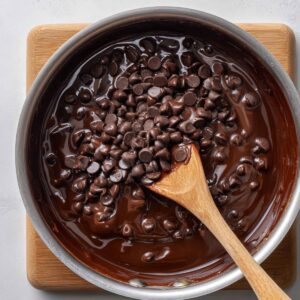 Melting chocolate in saucepan – A saucepan filled with melting chocolate and chocolate chips, being stirred with a wooden spoon.