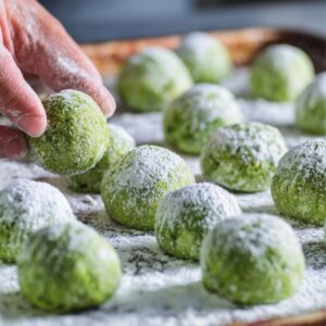 Close-up of hands shaping matcha cookie dough into small balls and rolling them in powdered sugar before baking.