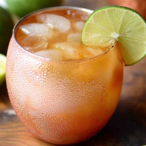 Copper mug Moscow Mule Recipe filled with ice and topped with a lime wedge, surrounded by fresh limes and peaches on a wooden board.