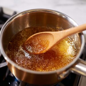Saucepan of bubbling golden sugar syrup, stirred with a wooden spoon.
