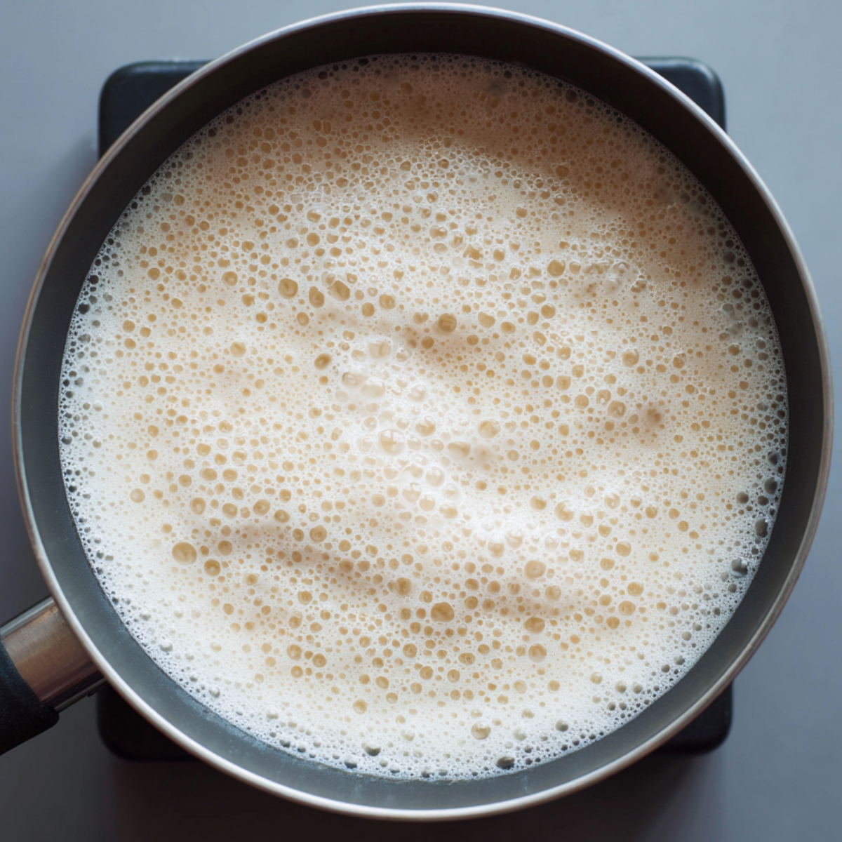 A saucepan filled with hot frothy milk, small bubbles covering the surface, just below simmering point.