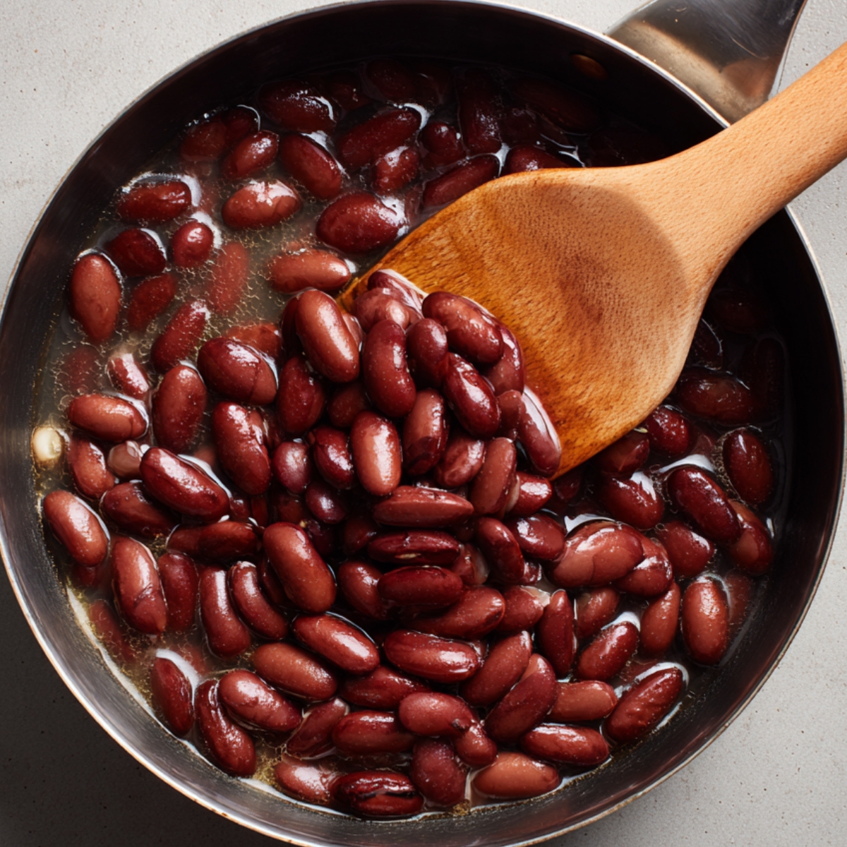 Cooked red kidney beans in a saucepan being stirred with a wooden spoon.
