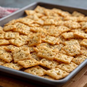 A baking sheet covered with a single layer of seasoned crackers, ready for baking.
