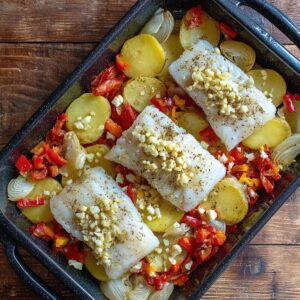 Prepared ingredients: raw cod fillets, sliced potatoes, red bell pepper, and chopped onions with seasonings.