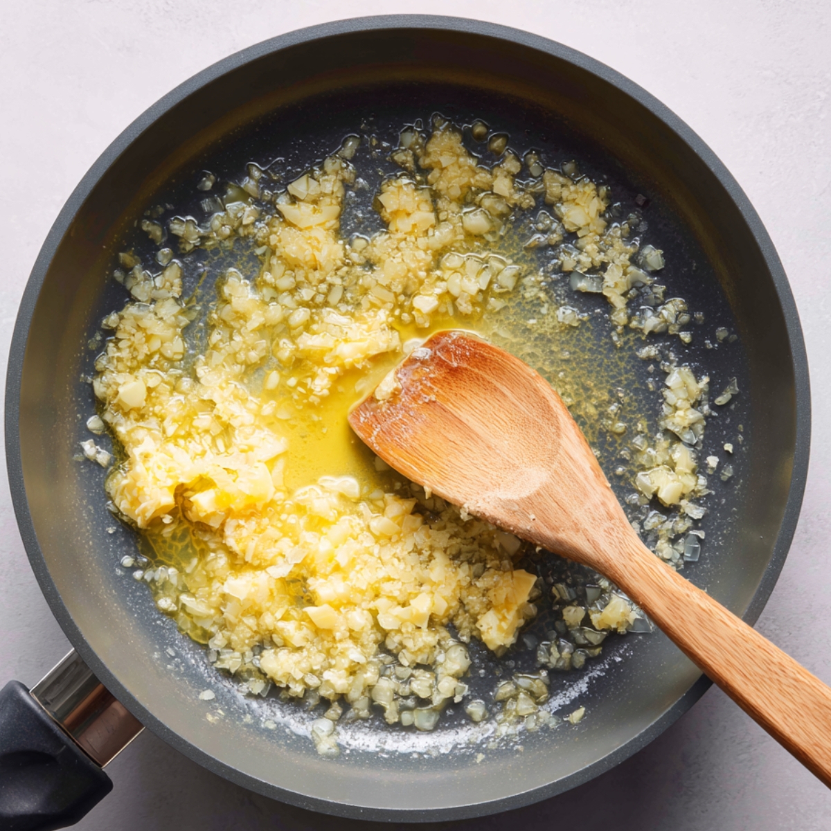 Minced garlic being sautéed in melted butter in a frying pan, stirred with a wooden spoon.
