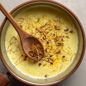 Rabri preparation: A saucepan of creamy milk with saffron strands and cardamom, stirred with a wooden spoon.