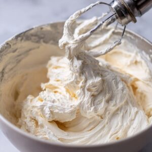 Cream cheese filling: A mixing bowl filled with smooth whipped cream cheese mixture with a hand mixer.