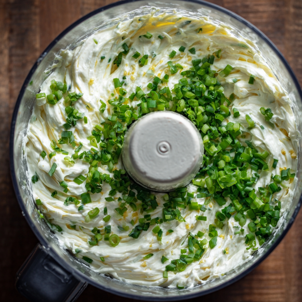A food processor containing a creamy white mixture (cream cheese base) topped with finely chopped green onions.