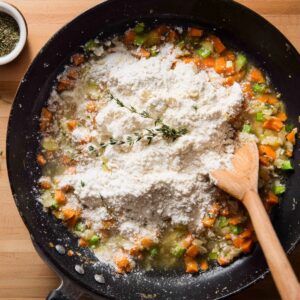Easy Bacon Cheddar Gnocchi Soup Recipe 19 Vegetables and flour in skillet – Chopped carrots, celery, and onions in bacon fat with flour sprinkled over, being stirred with a wooden spoon.