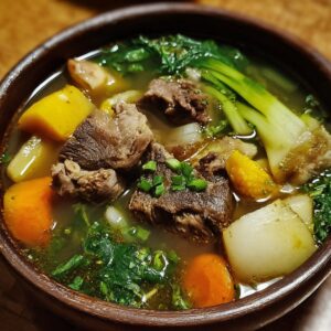 Bowl of beef soup — A rustic wooden bowl filled with clear beef broth, chunks of tender beef, carrots, corn, potato, and leafy greens, topped with chopped scallions.