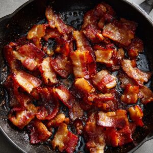 A cast-iron skillet with crispy bacon pieces cooked until golden brown.