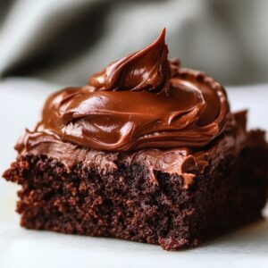 Close-up of a single thick brownie square topped with a generous swirl of glossy chocolate frosting.