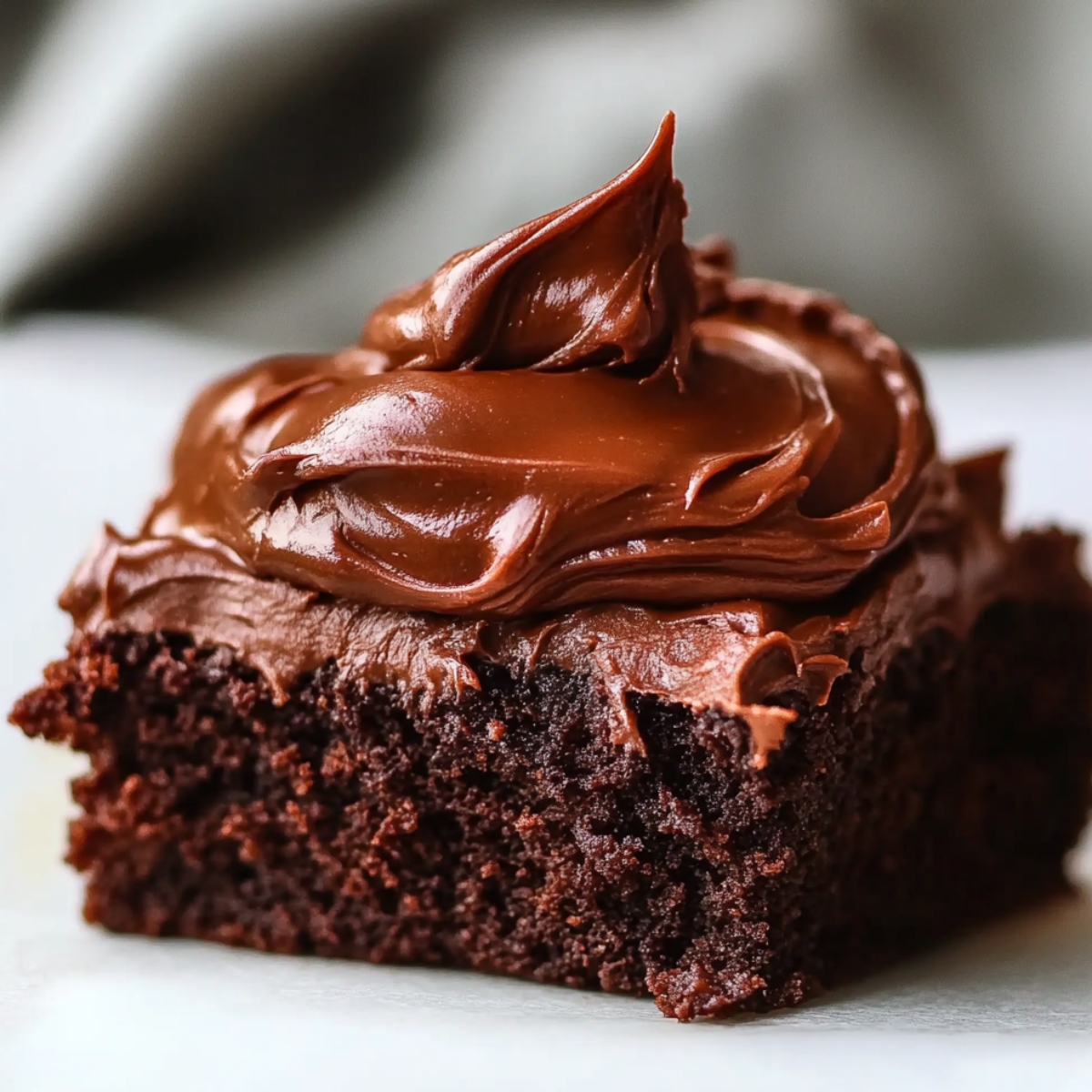 Close-up of a single thick brownie square topped with a generous swirl of glossy chocolate frosting.
