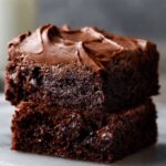 Two stacked fudgy Brownie Frosting recipe topped with creamy chocolate frosting on a marble surface