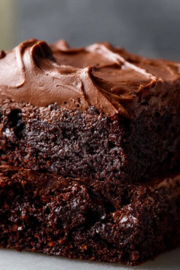 Two stacked fudgy Brownie Frosting recipe topped with creamy chocolate frosting on a marble surface