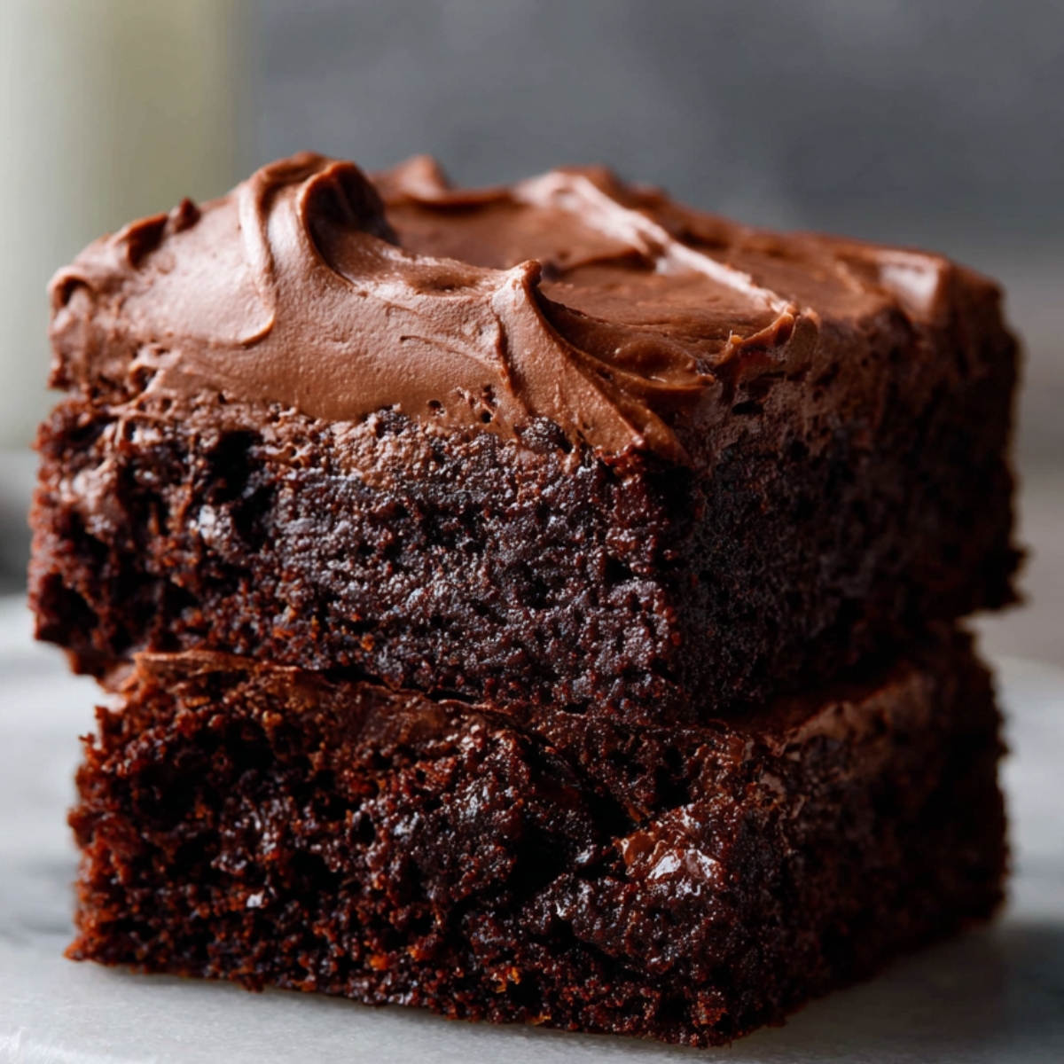 Two stacked fudgy Brownie Frosting recipe topped with creamy chocolate frosting on a marble surface