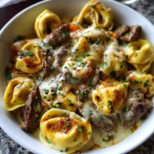 Best Cheesesteak Tortellini Provolone Sauce Recipe 16 A bowl of tortellini pasta mixed with tender steak pieces, smothered in creamy provolone sauce, and sprinkled with parsley.