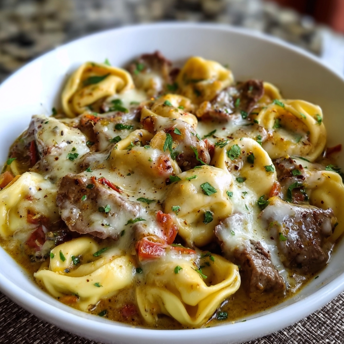 A bowl of Cheesesteak Tortellini Provolone Sauce mixed with tender steak pieces, smothered in creamy provolone sauce, and sprinkled with parsley.