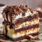 A decadent slice of chocolate Elvis Presley Cake Recipes, rich with layers of moist, dark sponge, creamy frosting, and a generous drizzle of chocolate sauce, topped with finely shaved chocolate.