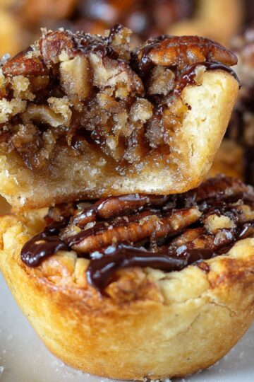 Pecan tassies on a plate with a bite taken out, showing a soft, nutty interior and a crisp crust.