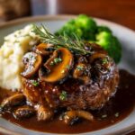 A delicious plate of Salisbury steak is served with mashed potatoes and a savory brown gravy. The steaks are topped with onions and the rich sauce, making for a comforting, hearty meal.