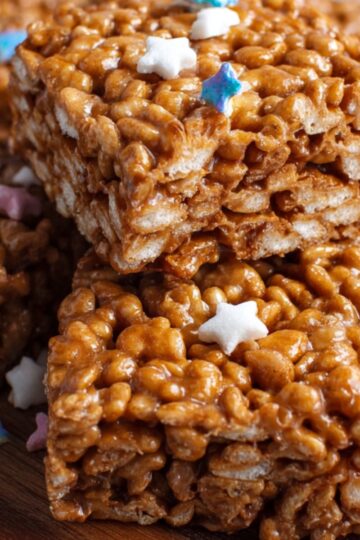 A close-up of a Star Crunch Recipe of Rice Krispies treats, decorated with small star-shaped pastel sprinkles on top, arranged on a wooden tray.