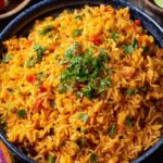 A vibrant tawa pulao of rice with cilantro and garnished with chopped tomatoes, served alongside lime wedges, suggesting a flavorful and fresh rice dish, possibly pilaf or seasoned rice.