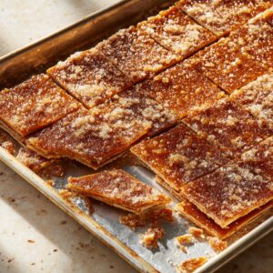 A baking tray filled with freshly baked caramelized toffee squares sprinkled with sugar crystals, cooling and glistening in the light.