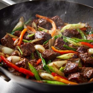 Protein, likely chicken or beef, being tossed into a hot wok, with vegetables in the background