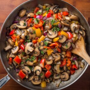 A sautéed vegetable mix of mushrooms, bell peppers, onions, and herbs in a skillet, likely part of the preparation for an omelette or frittata.